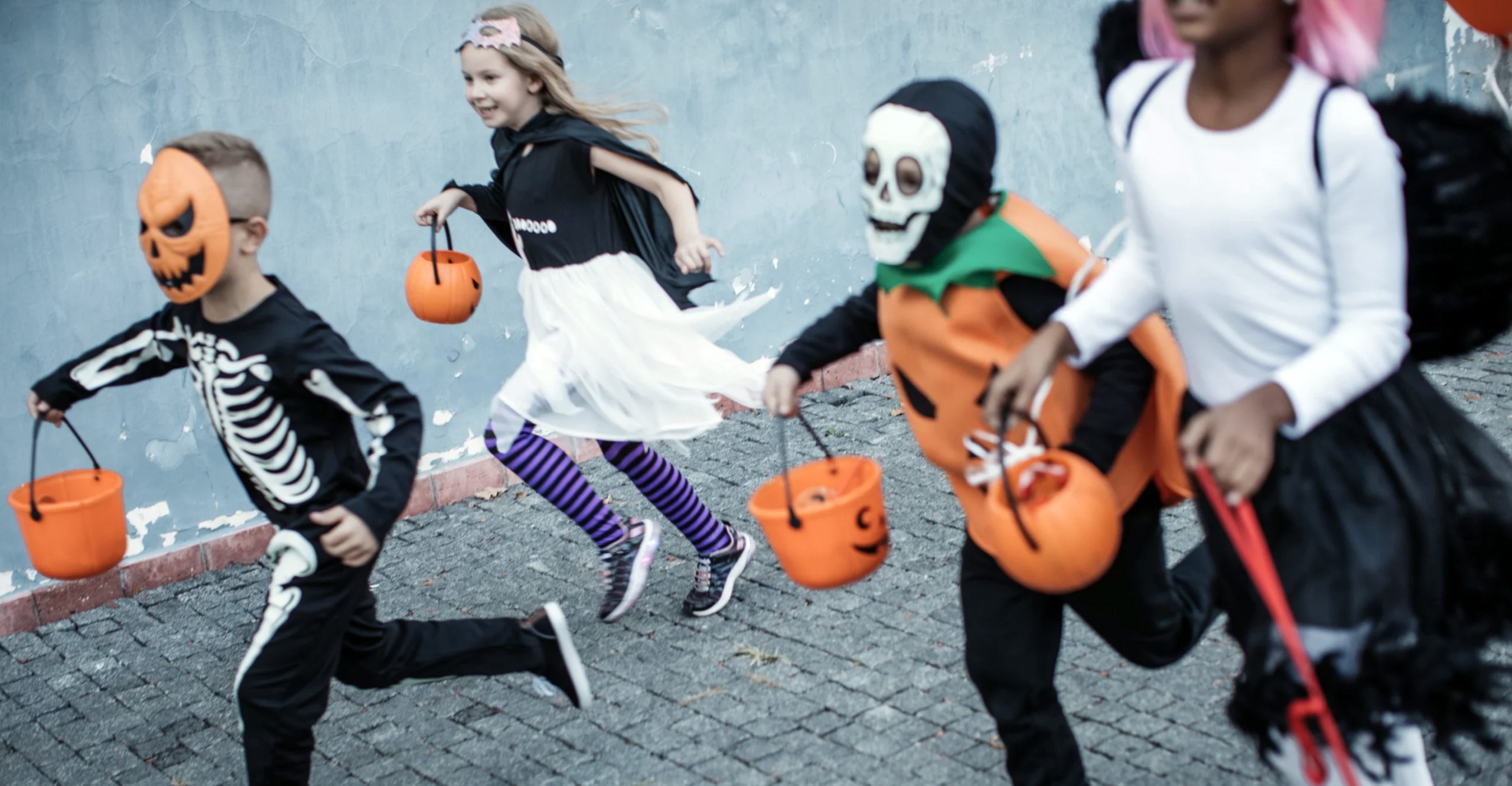 A group of children are dressed as skeletons and running down a street.